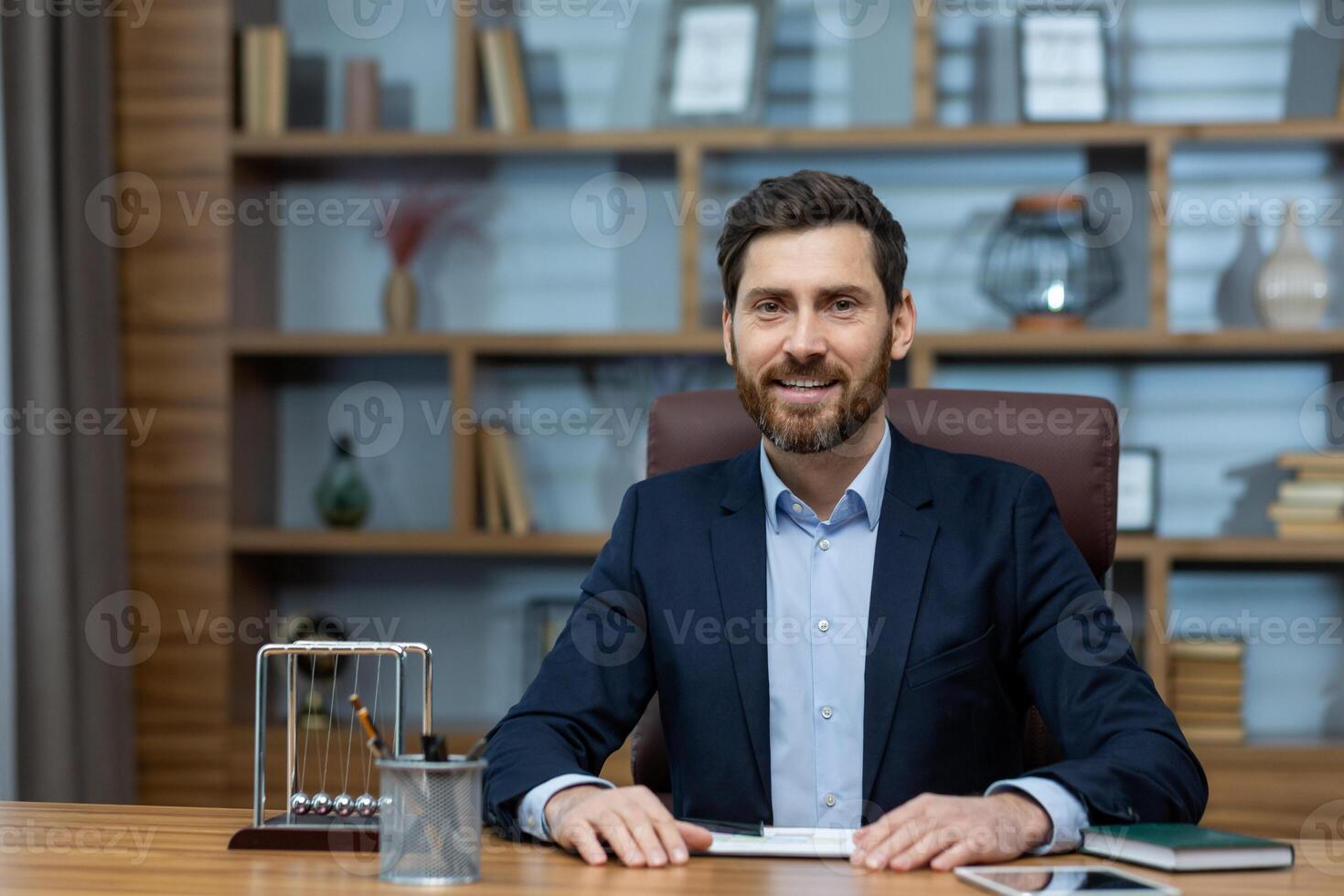 Confident mature male executive with a friendly smile, working at his neat home office desk, dressed in a business suit. photo