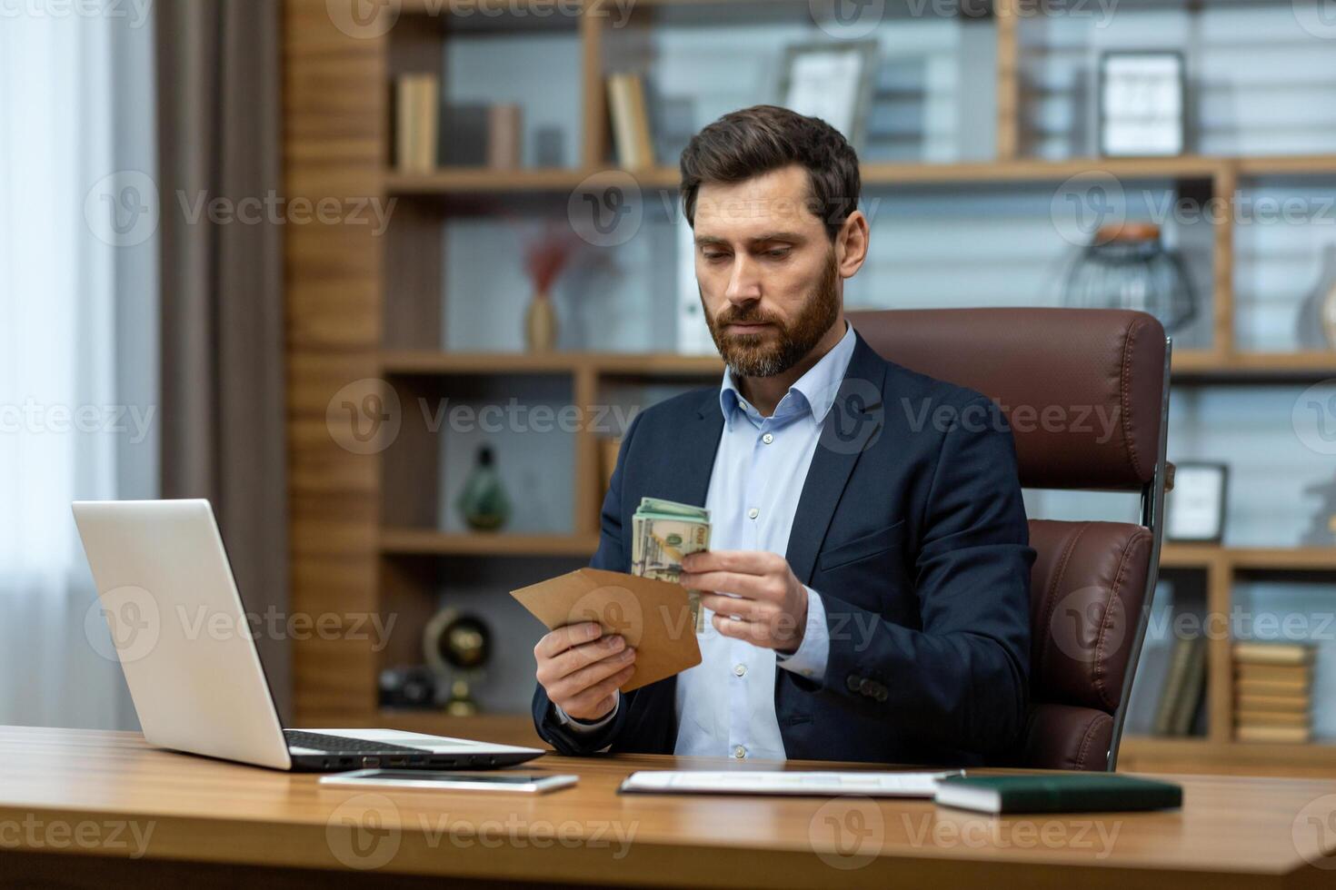 A focused mature businessman wearing a suit intently works in a home office setting, managing bills or finances. photo