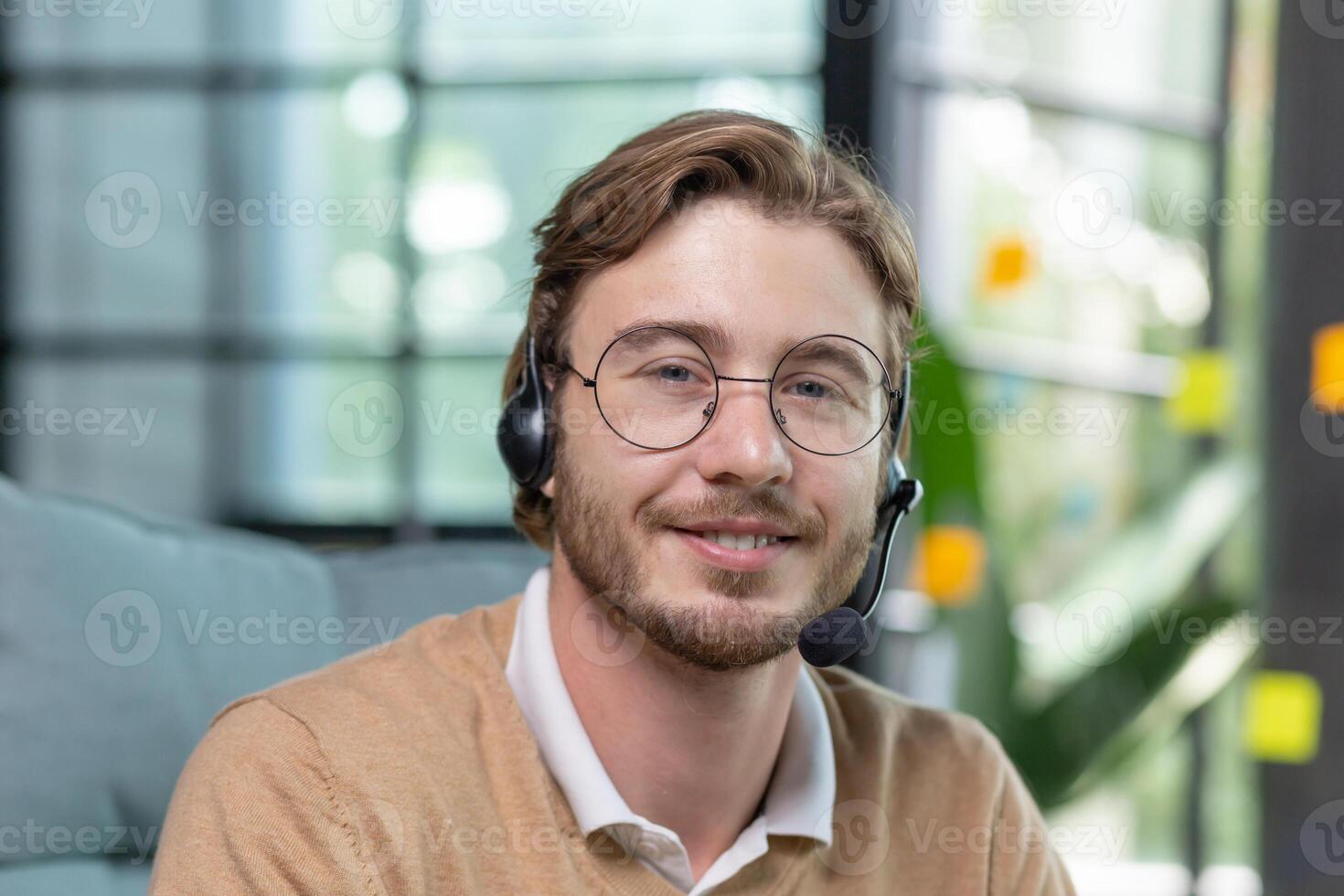 Close-up photo. Portrait of a young man in a headset and glasses, smiling and looking at the camera. photo