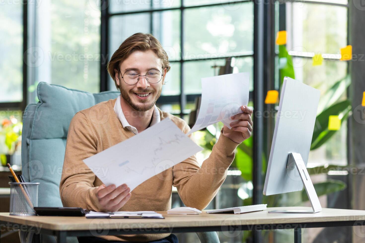 A young businessman, a freelancer works in a modern office with documents and papers. Sitting at a desk with a computer. photo