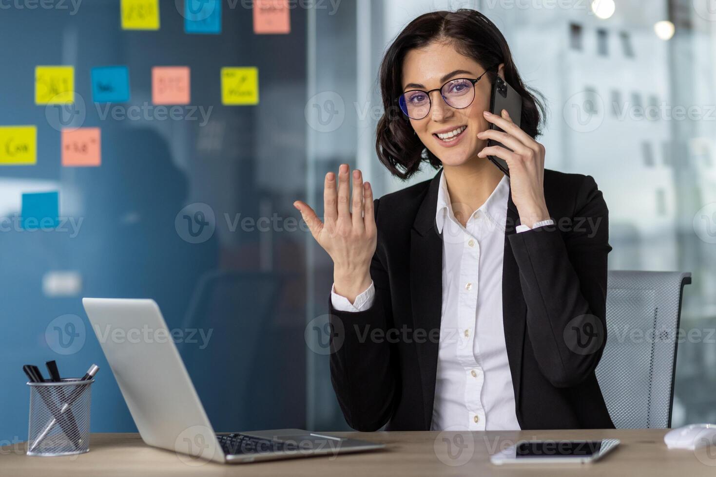 Confident businesswoman talking on phone while using laptop in a modern office. Professional attire and positive communication. photo