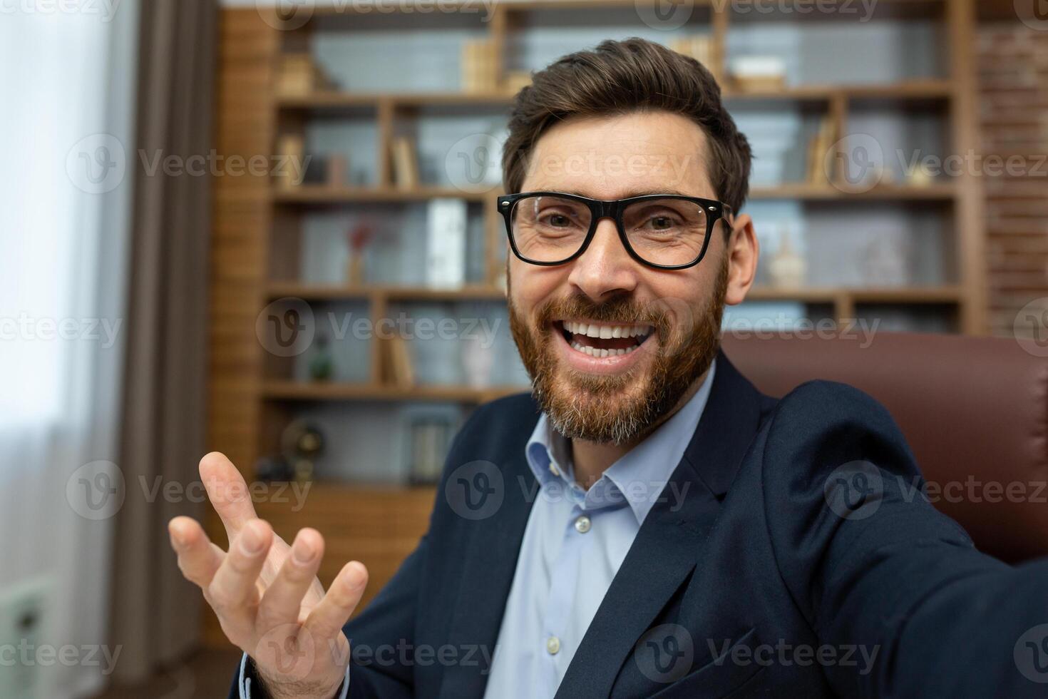 First person view of cheerful adult man in glasses having call with happy facial expression on luxury interior background. Excited office worker presenting new workplace with toothy smile. photo