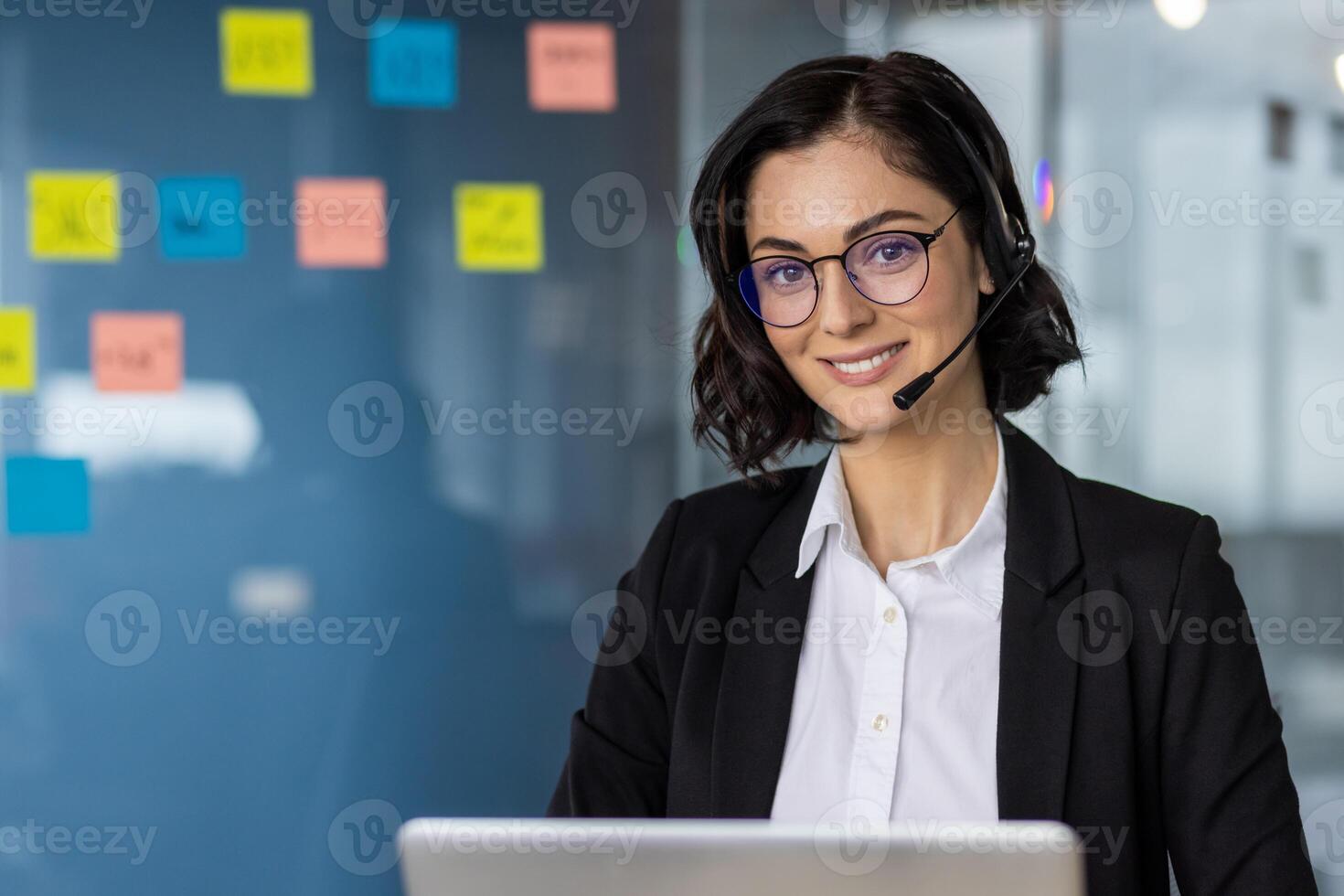 Smiling woman wearing headset working in modern office setting. Professional call center representative providing customer support, surrounded by colorful sticky notes. photo