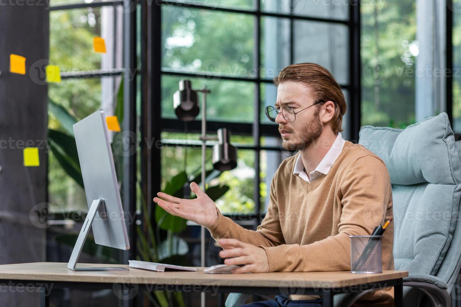 Frustrated and upset businessman reading news online from computer monitor, young blond man sad at workplace inside office in casual clothes unhappy with results. photo