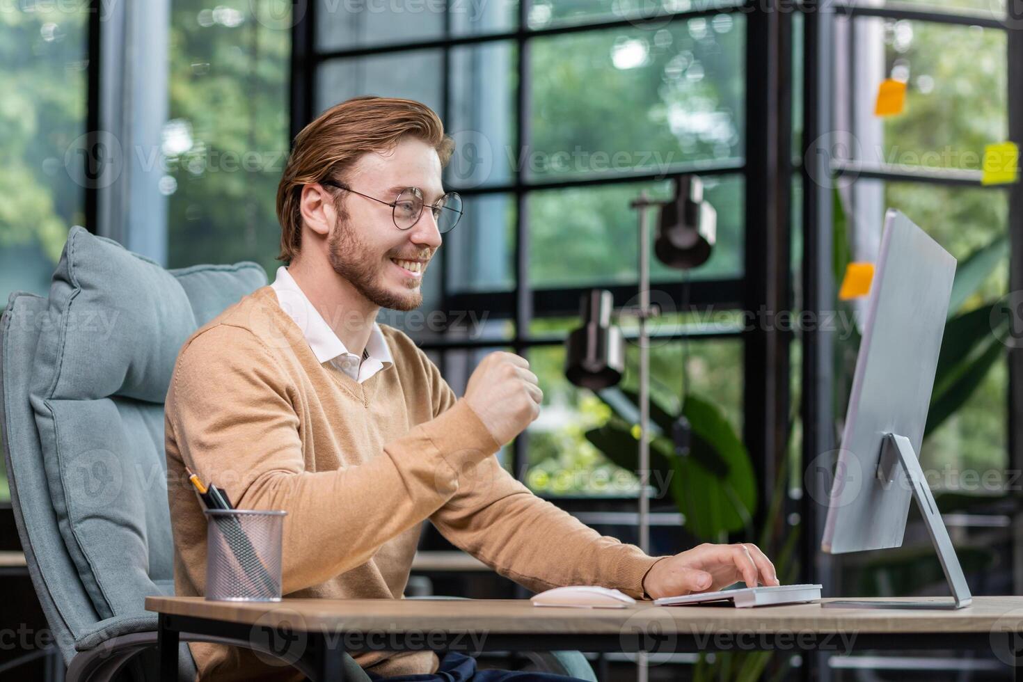 Young successful entrepreneur working inside office with computer, man in casual clothes smiling and typing on keyboard, businessman happy with achievement results and income. photo