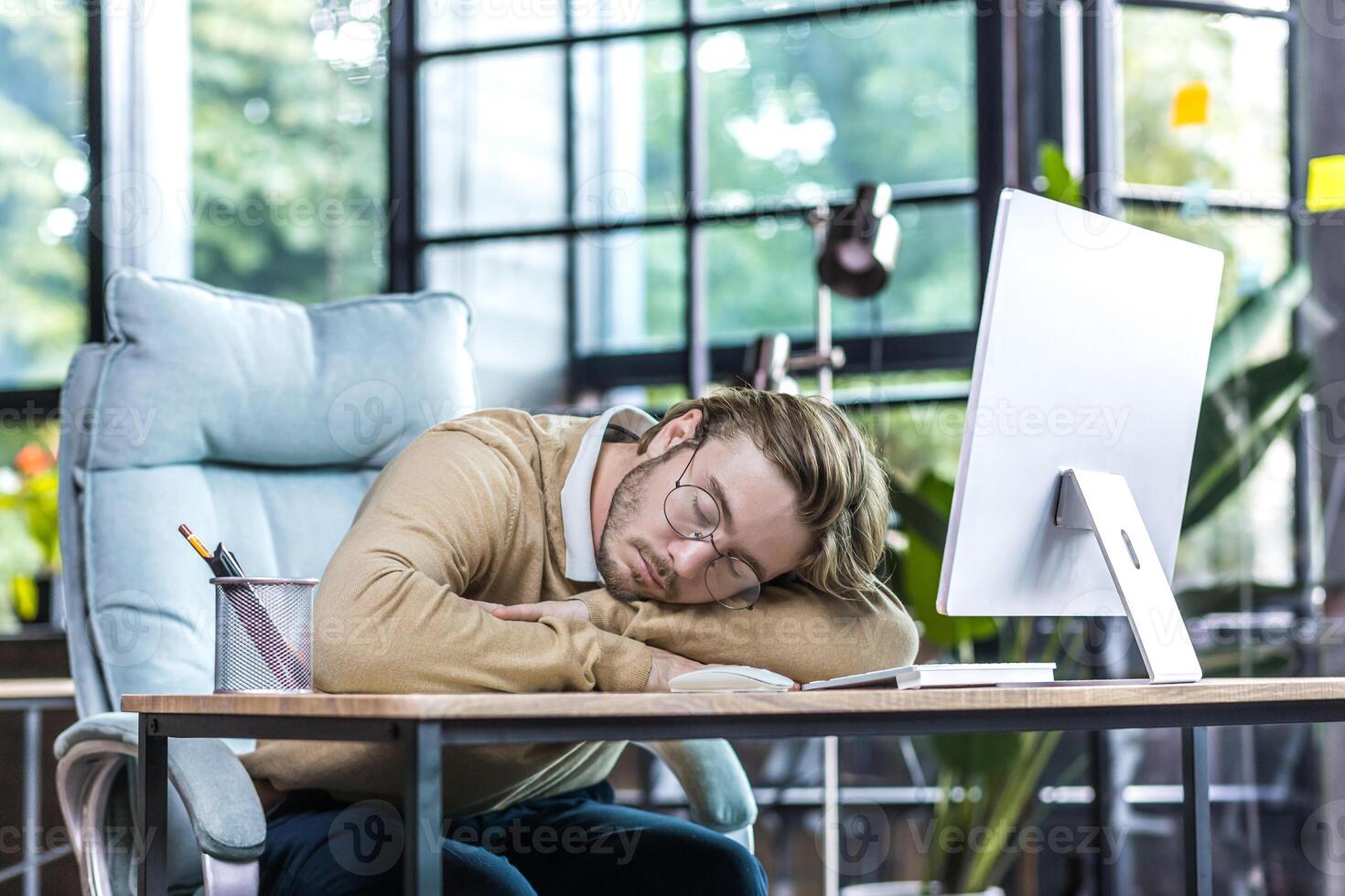 Young businessman resting in office, man in glasses sleeping on table, freelancer using computer, daytime sleep photo