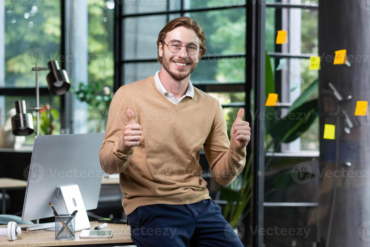 Portrait of happy blond man inside office, man in casual clothes smiling and looking at camera, young successful businessman showing thumbs up at camera, programmer at work with computer. photo
