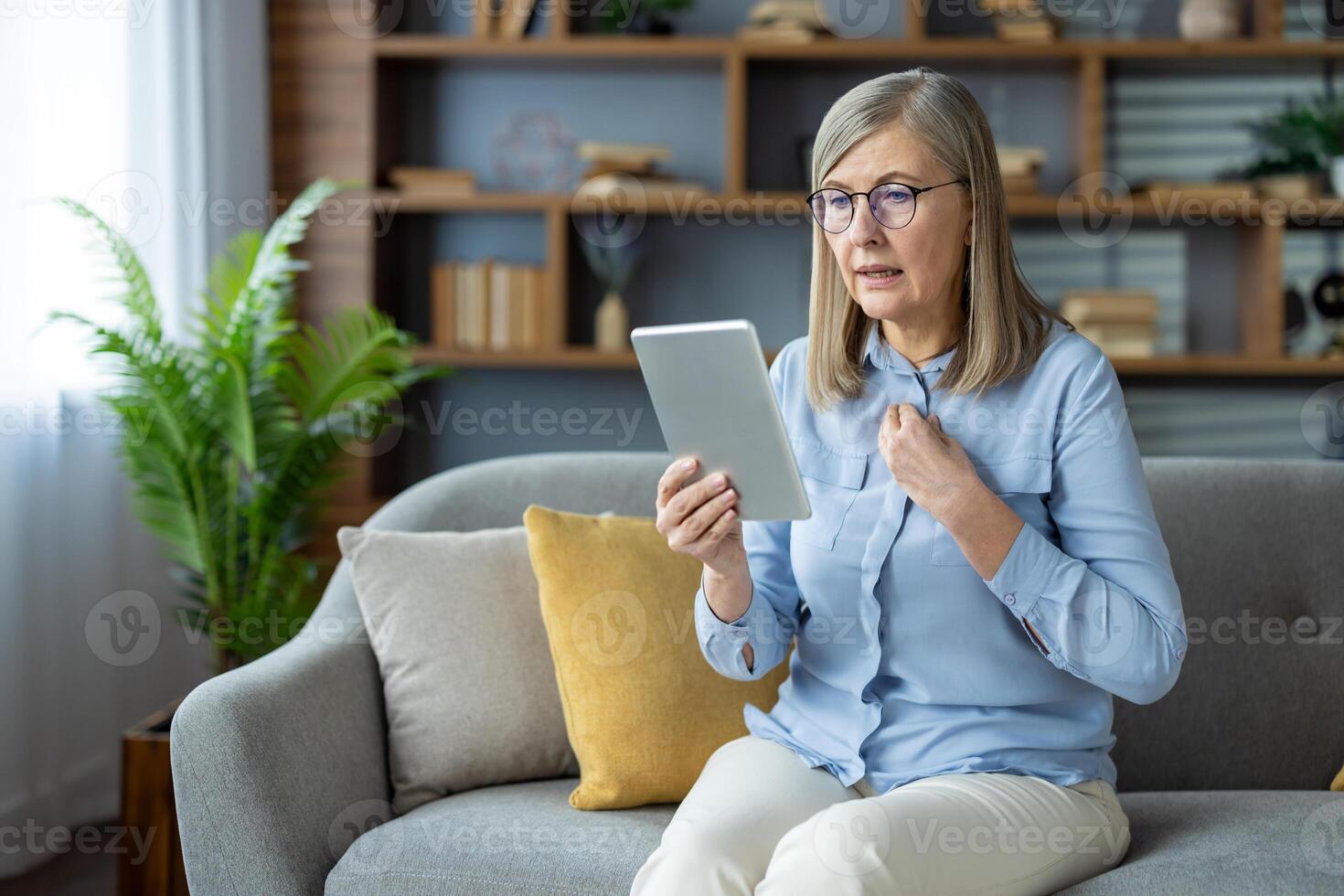 An elderly woman engages in virtual consultation with psychologist, displaying frustration and concern while sitting on sofa at home. Concept includes mental health, online therapy photo
