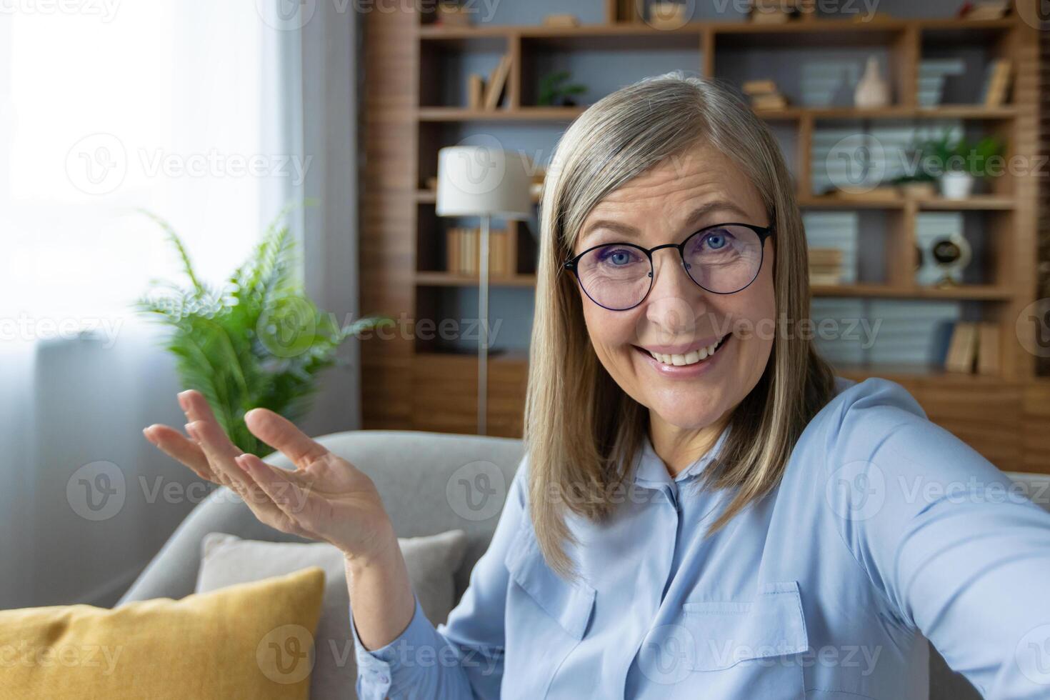 Smiling woman with glasses chatting on a call while waving. Home office in the background. Joyful and friendly communication. photo