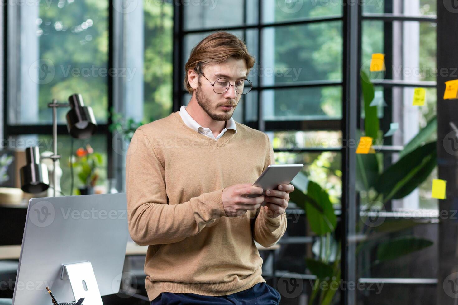 Portrait of a young male programmer who is standing in the office at the table and is concentrating on the tablet. photo