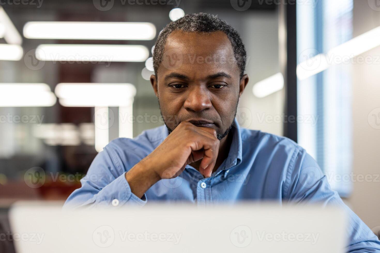 Professional businessman concentrating on tasks using laptop in modern office environment. Serious expression reflects deep thought. Ideal for themes emphasizing business, technology, productivity photo