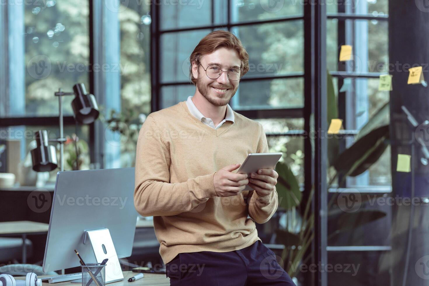 Portrait of young businessman businessman man blond smiling and looking at camera, at work in modern loft office, using tablet computer, IT specialist testing new software application photo