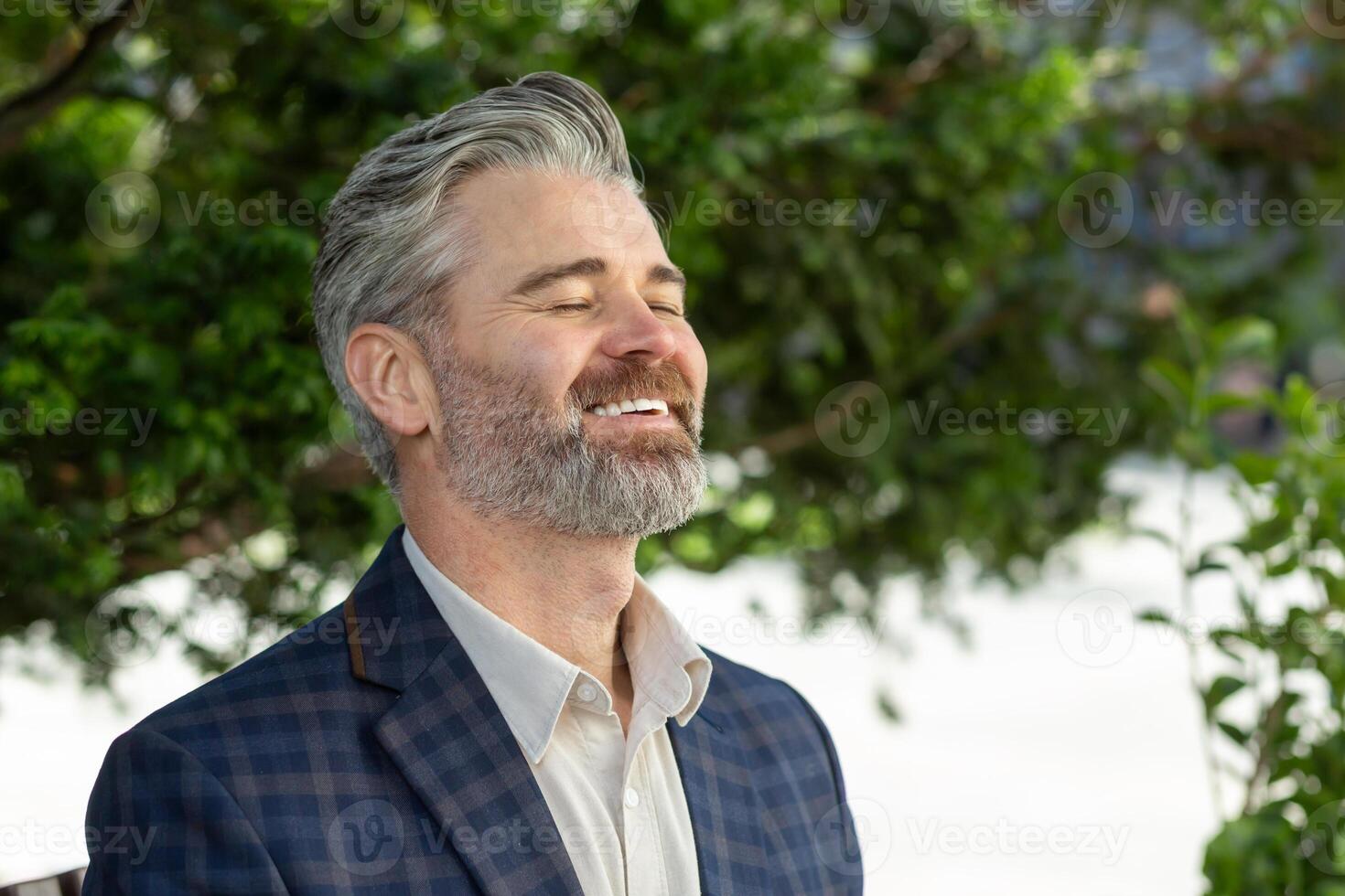 Portrait of a happy senior businessman in a suit, enjoying success outside an office environment with trees in the background. photo
