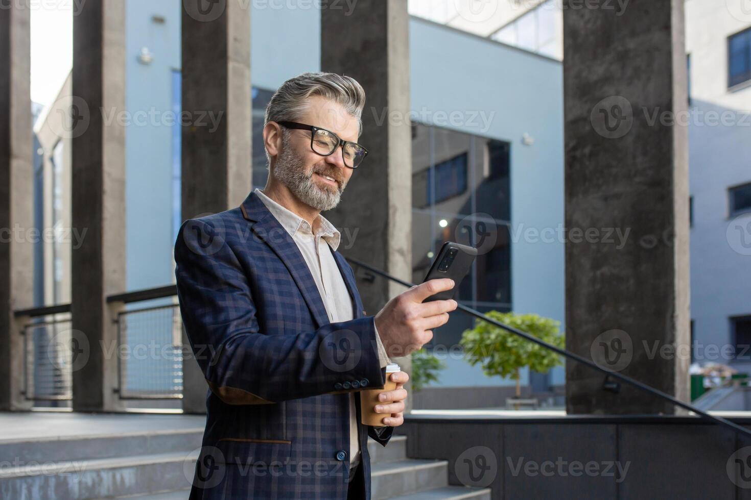 A distinguished senior businessman checks his smartphone while enjoying a coffee break outside a contemporary office structure. photo