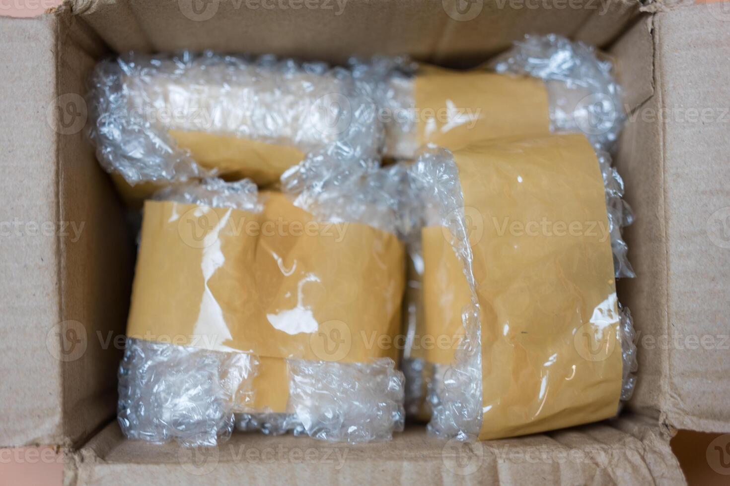 Packing fragile items with plastic air bubble wrapped and adhesive tape in box. photo