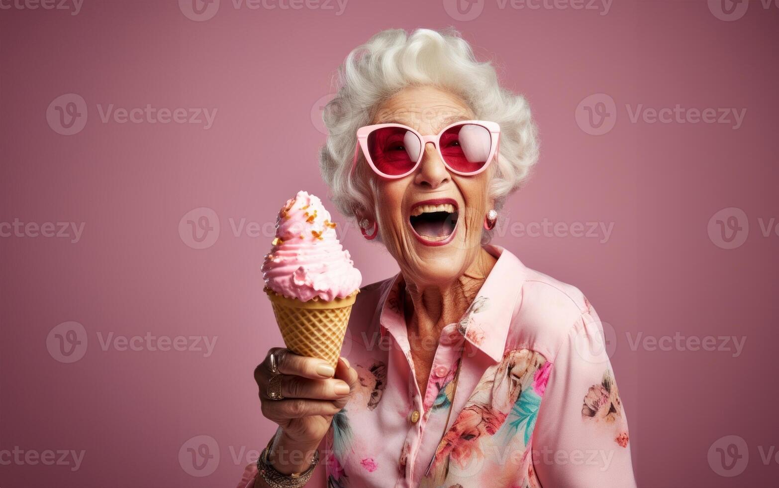 An elegant older woman, adorned with stylish sunglasses, enjoys a moment of indulgence as she savors ice cream, creating a vibrant and modern image against an isolated pink background photo