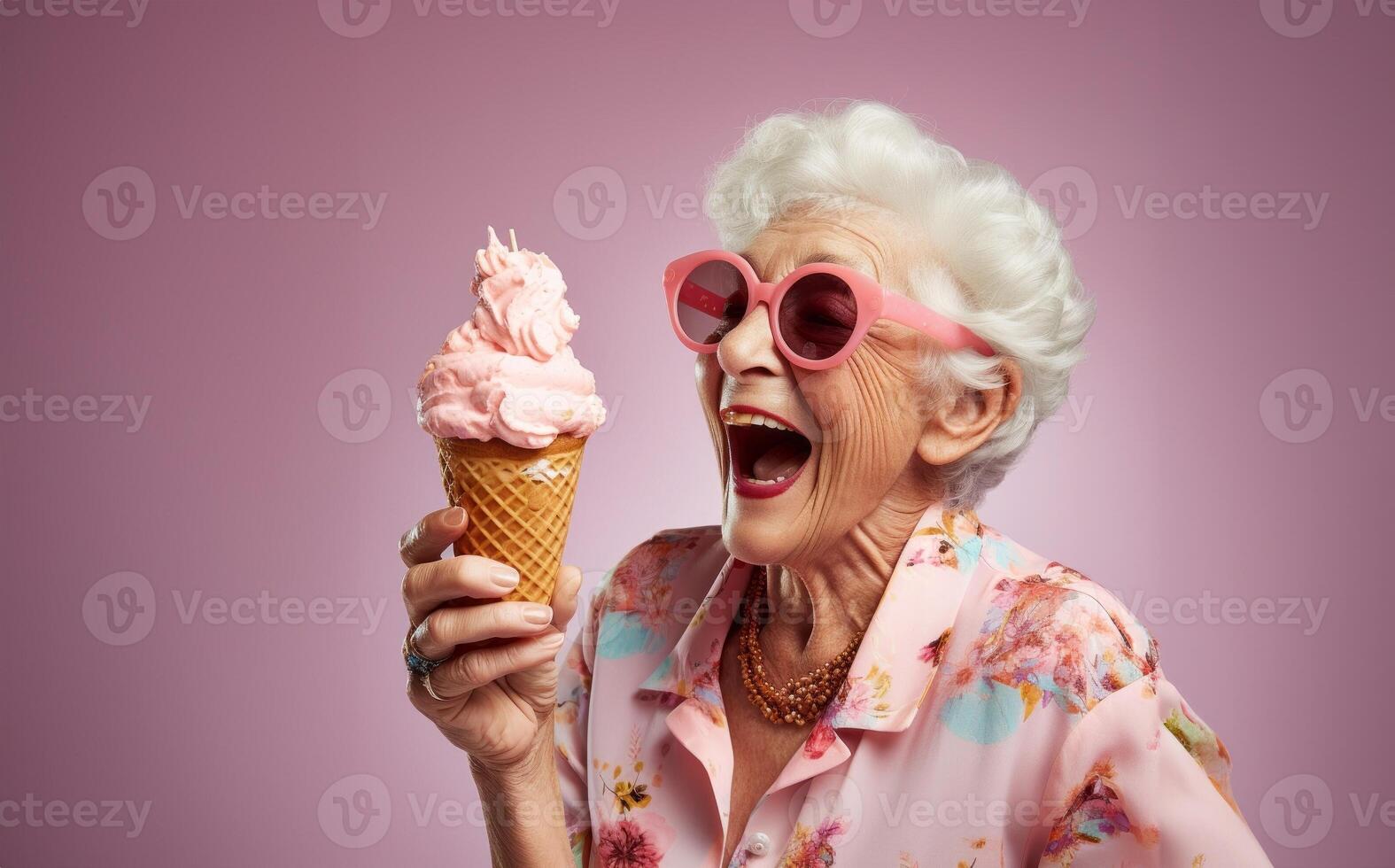 An elegant older woman, adorned with stylish sunglasses, enjoys a moment of indulgence as she savors ice cream, creating a vibrant and modern image against an isolated pink background photo