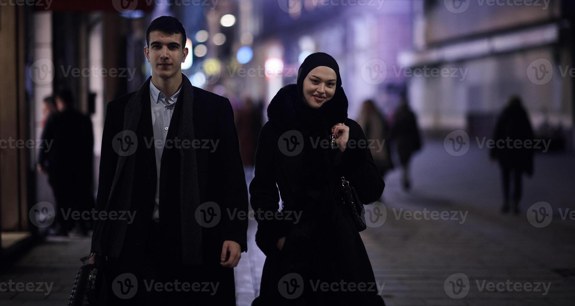 Happy multicultural business couple walking together outdoors in an urban city street at night near a jewelry shopping store window. photo