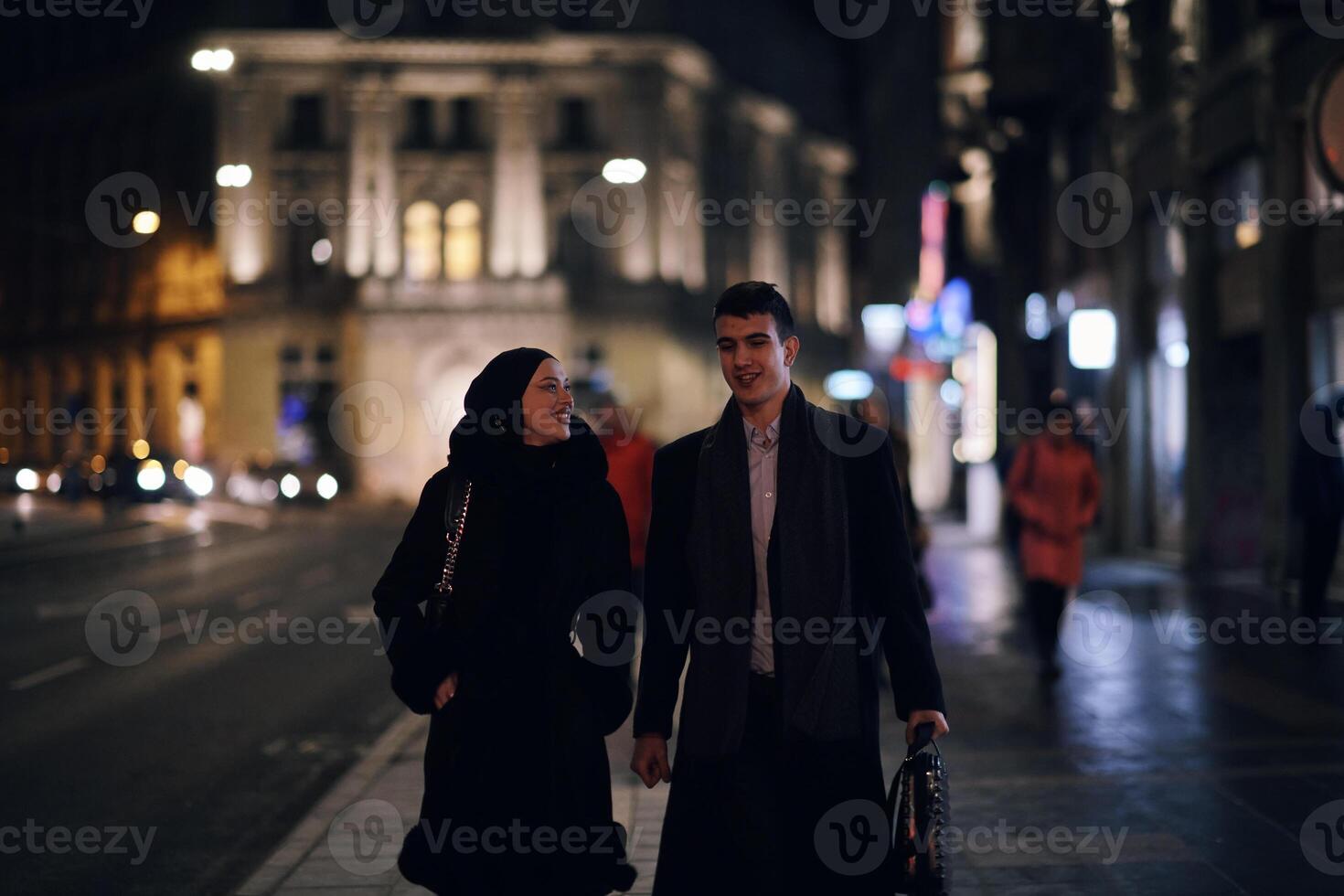 Happy multicultural business couple walking together outdoors in an urban city street at night near a jewelry shopping store window. photo