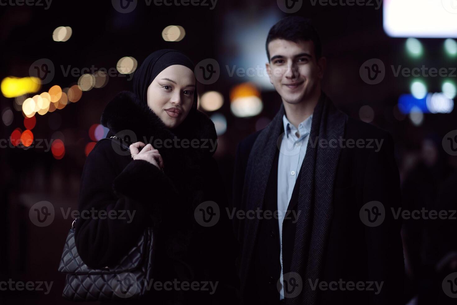 Happy multicultural business couple walking together outdoors in an urban city street at night near a jewelry shopping store window. photo