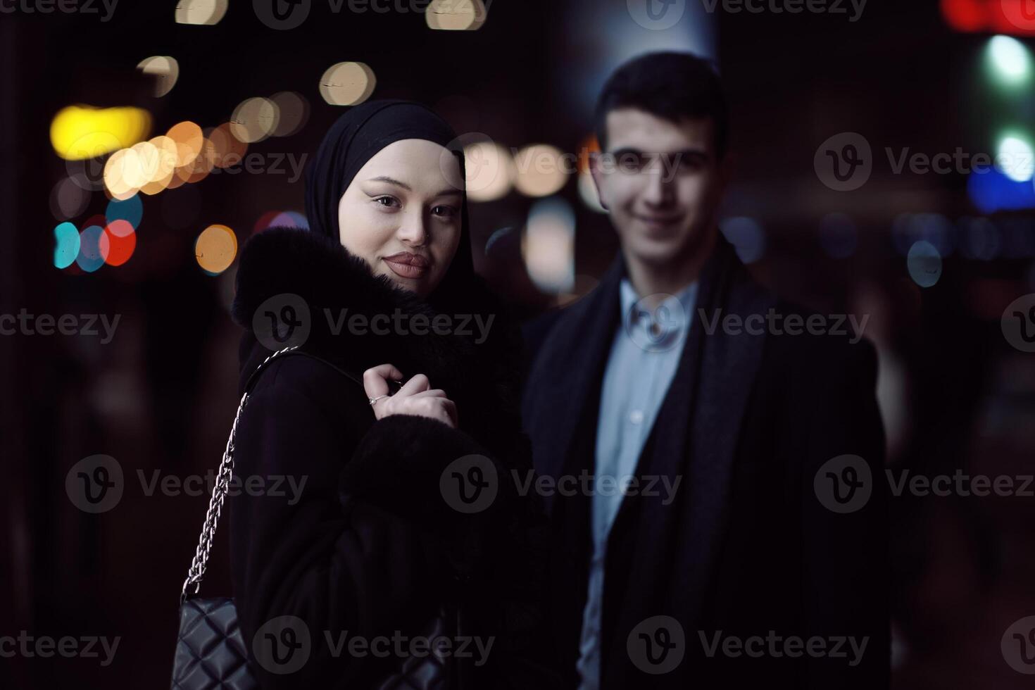 Happy multicultural business couple walking together outdoors in an urban city street at night near a jewelry shopping store window. photo