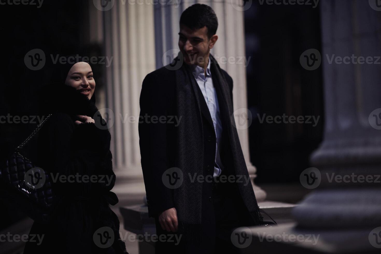 Happy multicultural business couple walking together outdoors in an urban city street at night near a jewelry shopping store window. photo