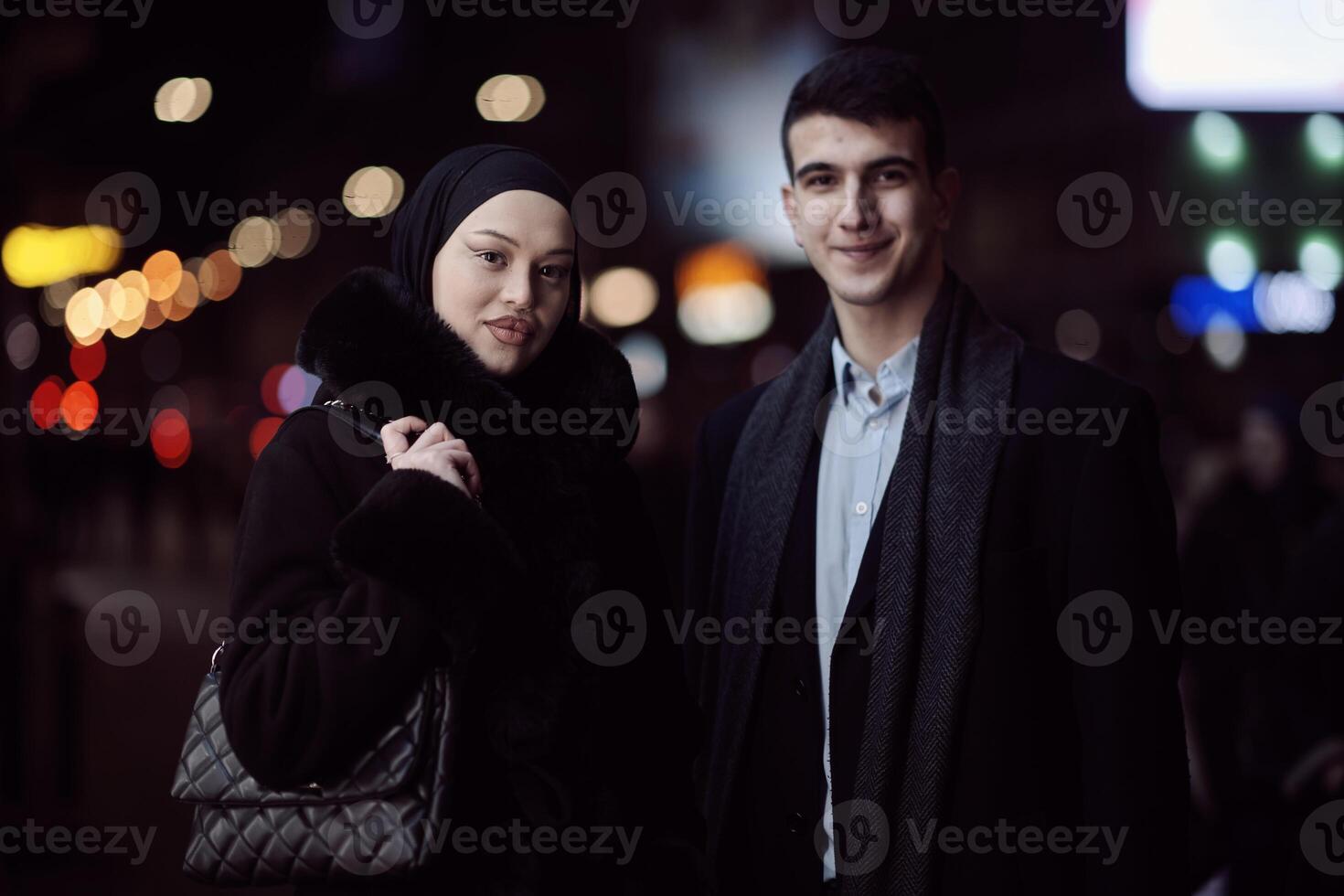 Happy multicultural business couple walking together outdoors in an urban city street at night near a jewelry shopping store window. photo