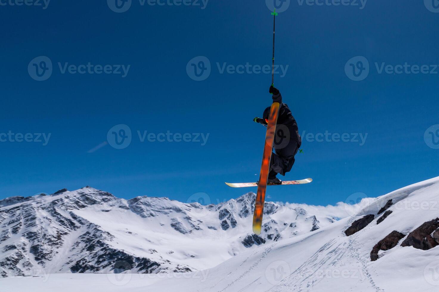 Freestyle skier performing a high jump with his skis crossed. High snow-capped mountains in the background photo