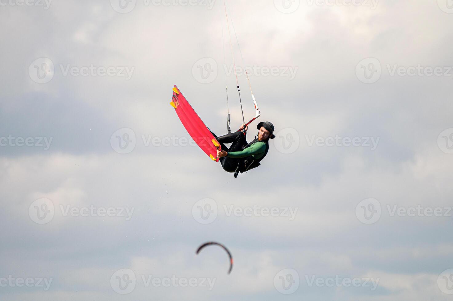 kitesurfer rides the waves at his home spot in the bay. An athlete in a panama hat performs a trick in the air while flying up against the background of a cloudy sky photo