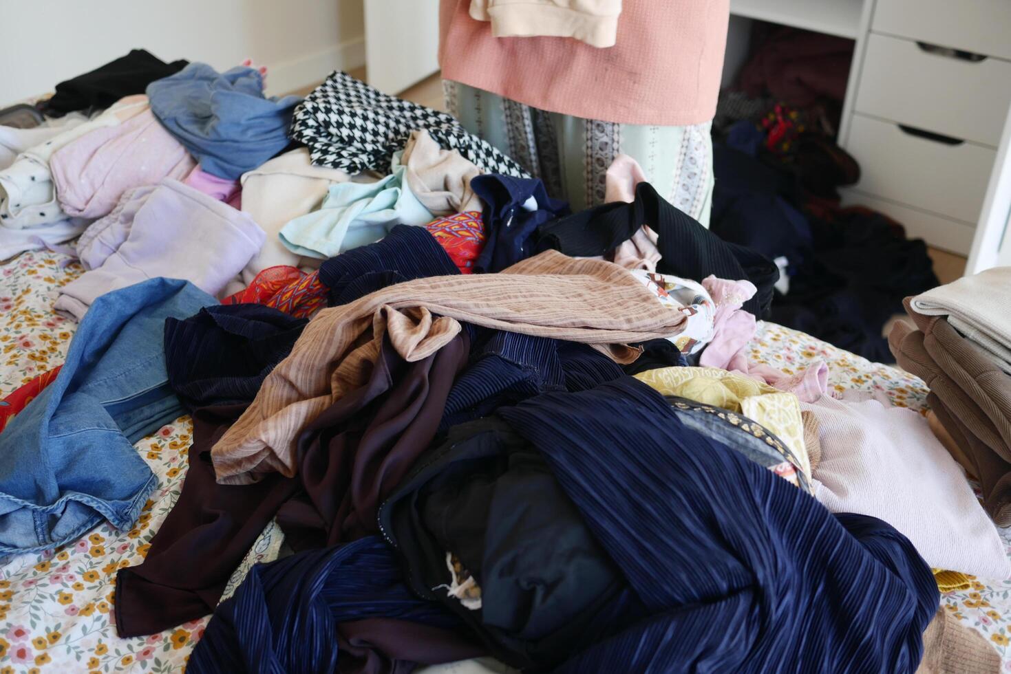 The bedroom is in a chaotic state, with clothes strewn across the bed and the floor photo