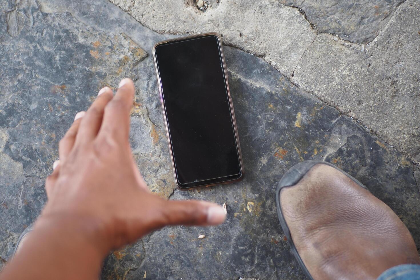 A person actively reaching downwards for their dropped phone that is on the ground photo