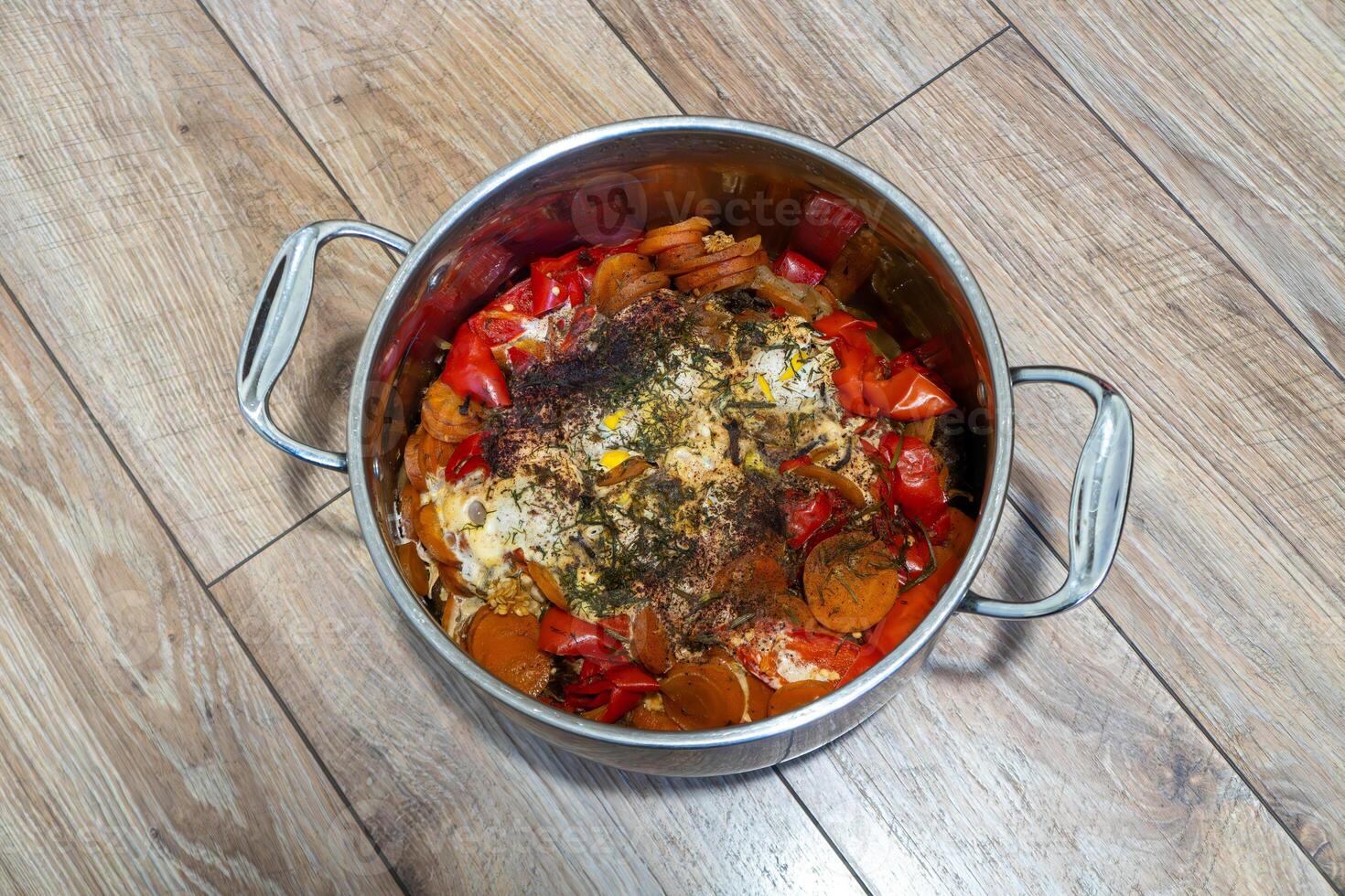 A stew with various vegetables in a metal pot. Photographed from above on a wooden floor. Concept of homemade cooking and healthy food photo