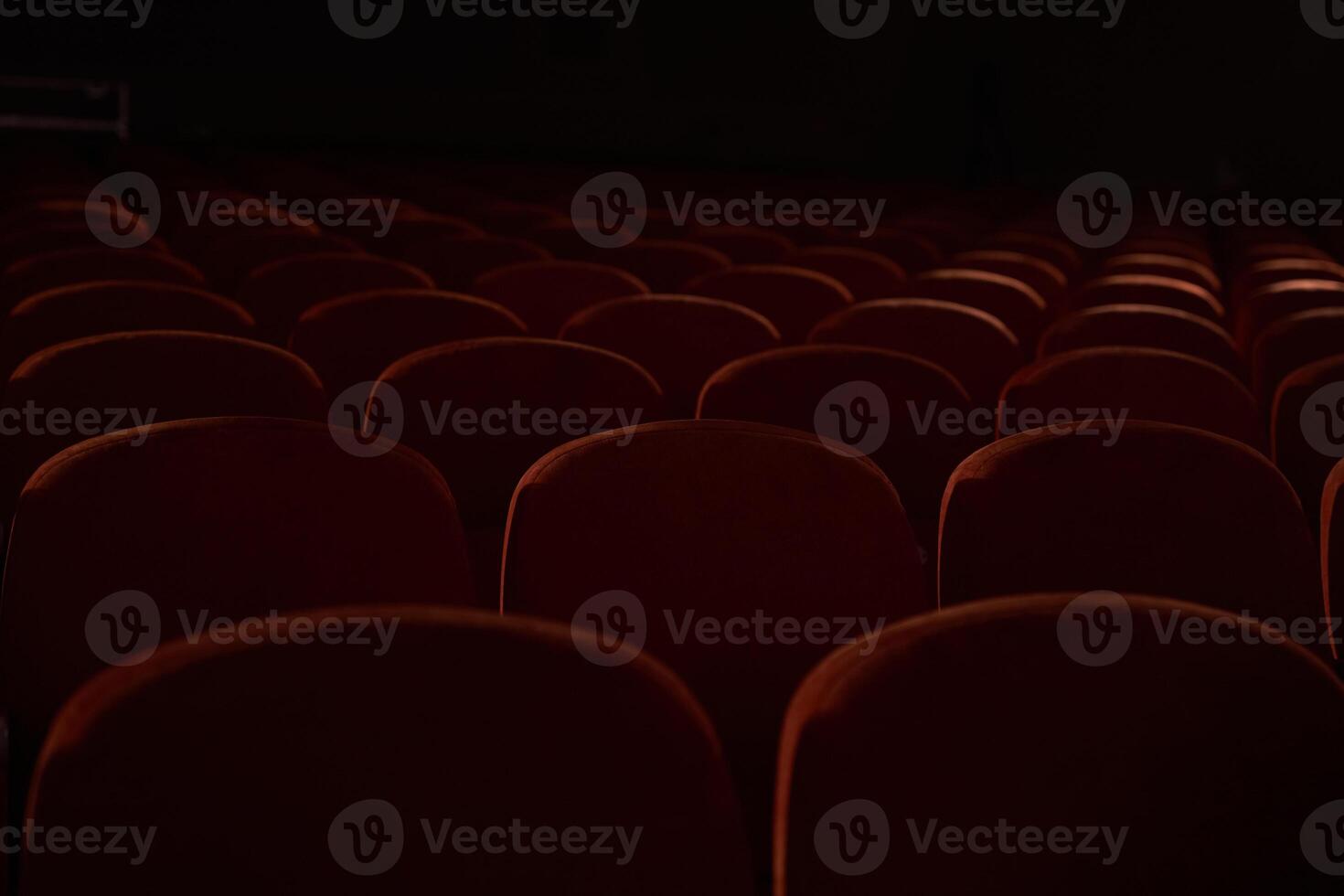 Close up of orange, red seats in dark empty cinema hall with copy space. Background with rows of chairs with selective focus. Concept of event, theatre, conference, show, presentation, audience photo