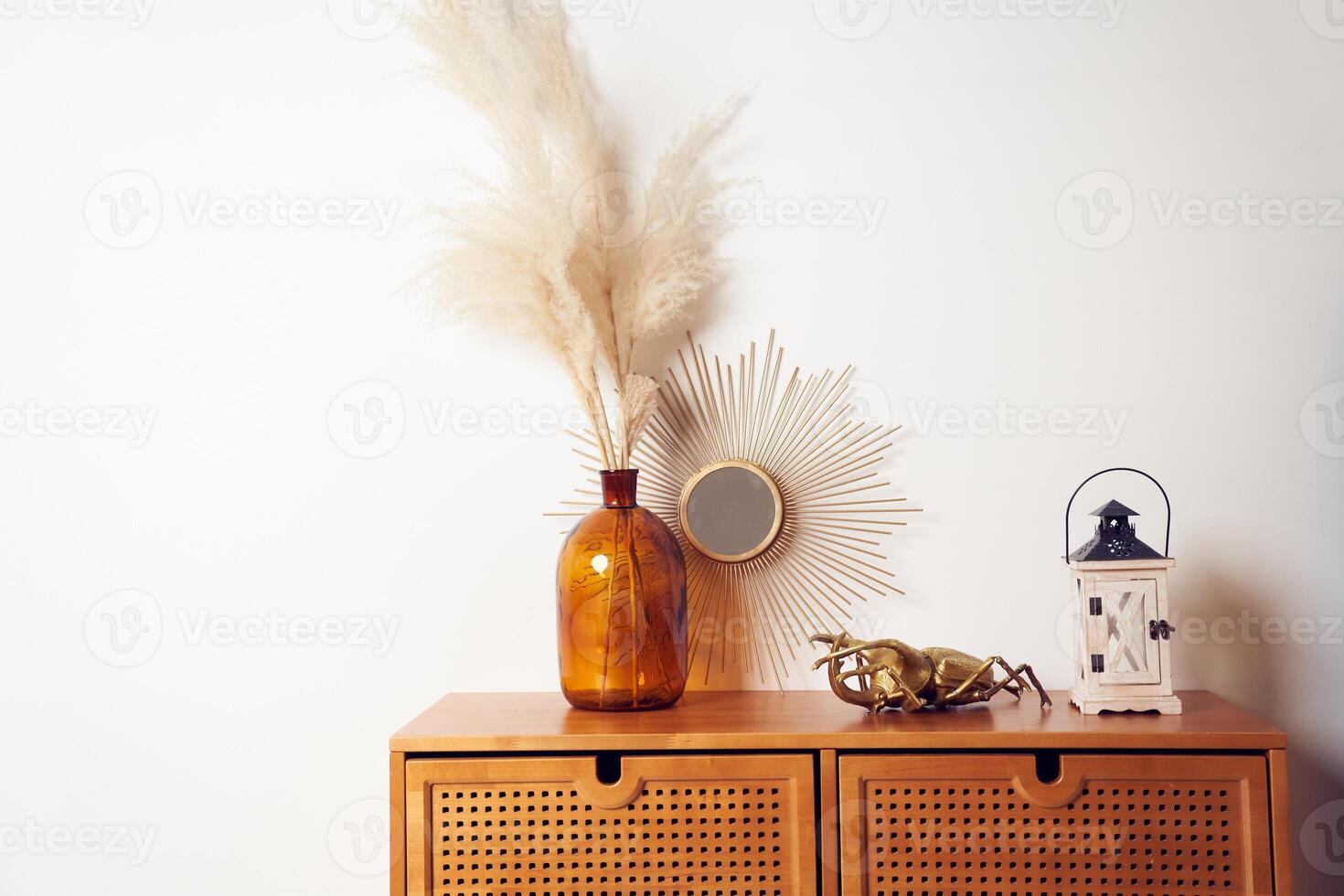 Bouquet of dried pampas grass flowers in a glass vase, mirrow, bronze figure of a beetle, wooden candle holder on brown drawers. Background with copy space, empty. Template, mockup for your design photo