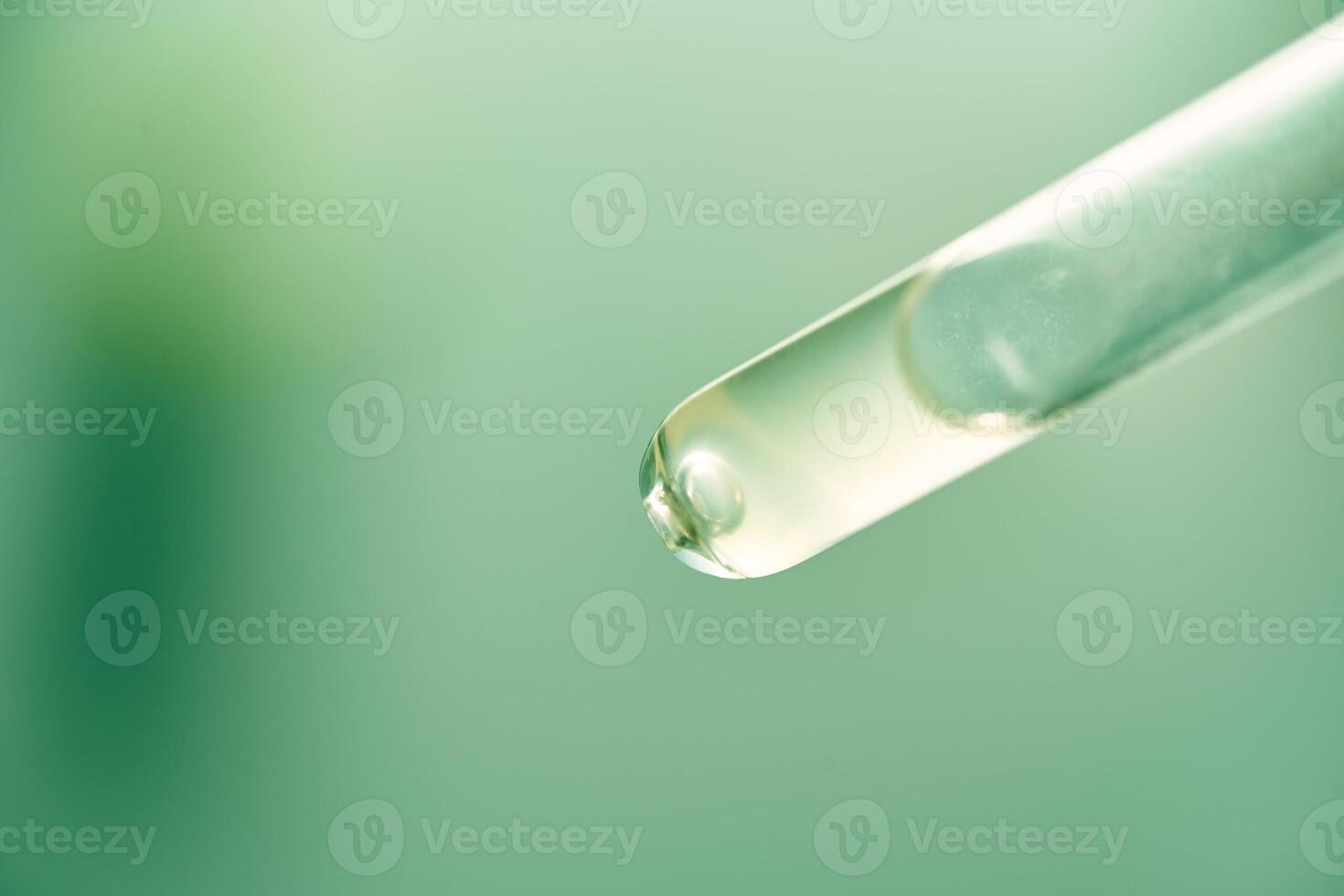 Cosmetic pipette with liquid close-up on a green background. Macro photography of a transparent glass pipette. Beauty concept, aromatherapy oil, medicine, vaccine development. photo