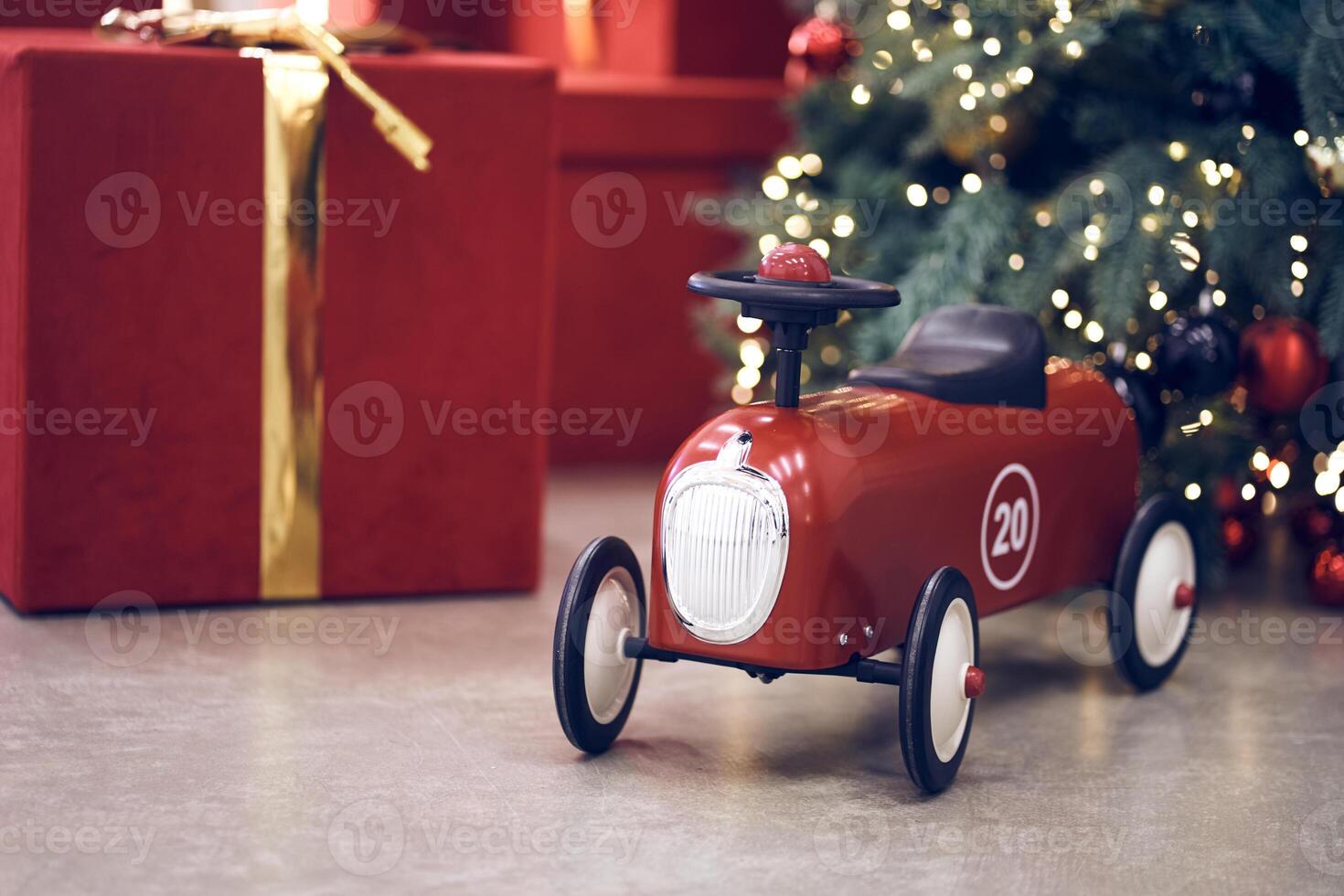 Side view of red children's retro car on the background of gifts in red boxes with golden bows, Christmas tree decorated garland, string light, red and blue balls. Background, copy space, bokeh photo