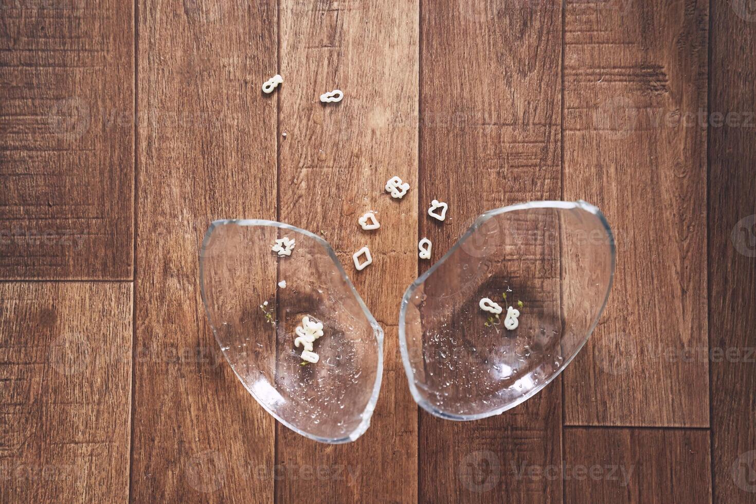 The transparent plate is divided into two parts. A cup of noodle soup in the form of figures for lunch fell on the wooden floor and broke. photo