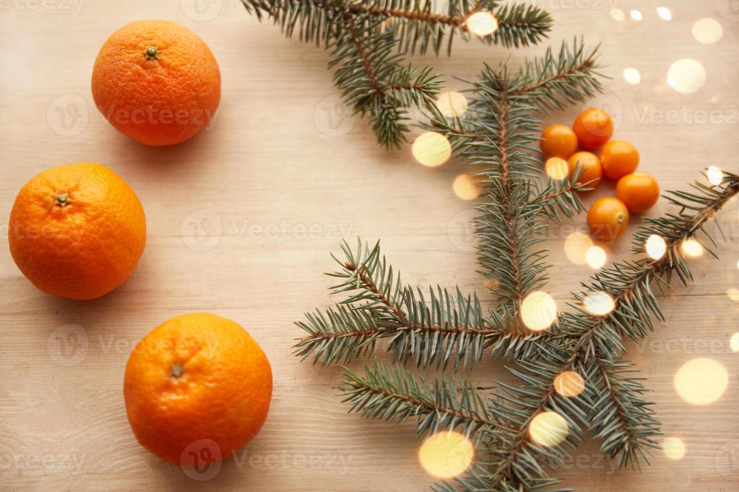 Fir branches with garlands on a light wooden background, decorated with tangerines and berries. View from above. Christmas concept photo