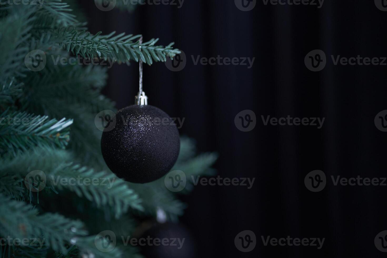 Close up of single black ball handing on christmas tree with bokeh. Christmas decor, black background with copy space. The concept of Christmas. Ball is on a pine branch of christmas tree photo