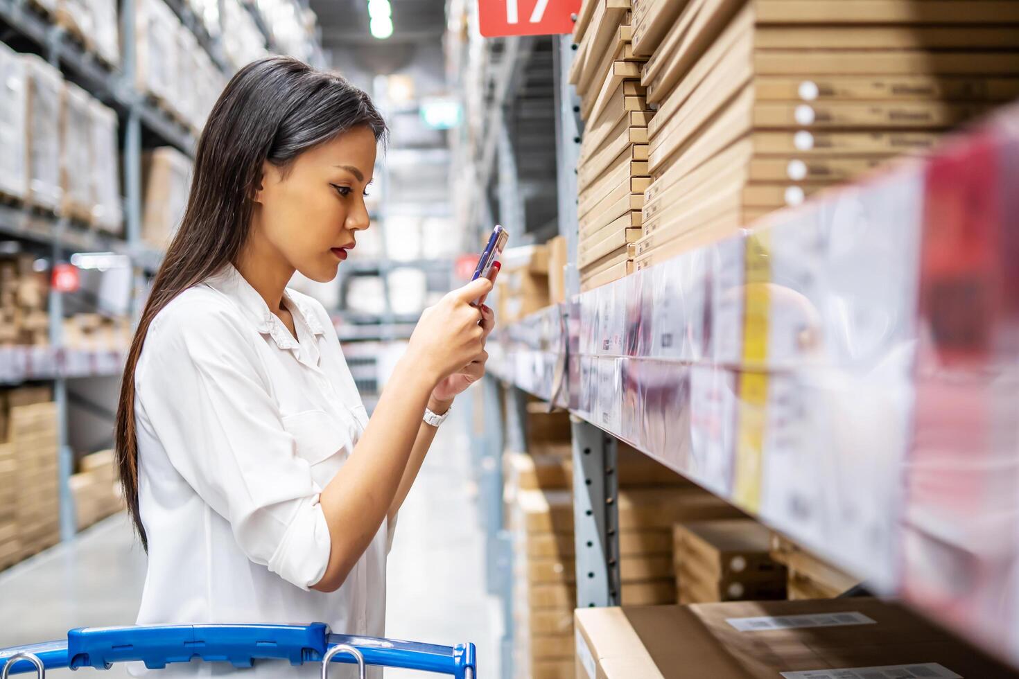 Young asian woman scanning the QR code via smart mobile phone for checking goods stock and price in warehouse, customer shopping and self service, The concept of modern technology photo