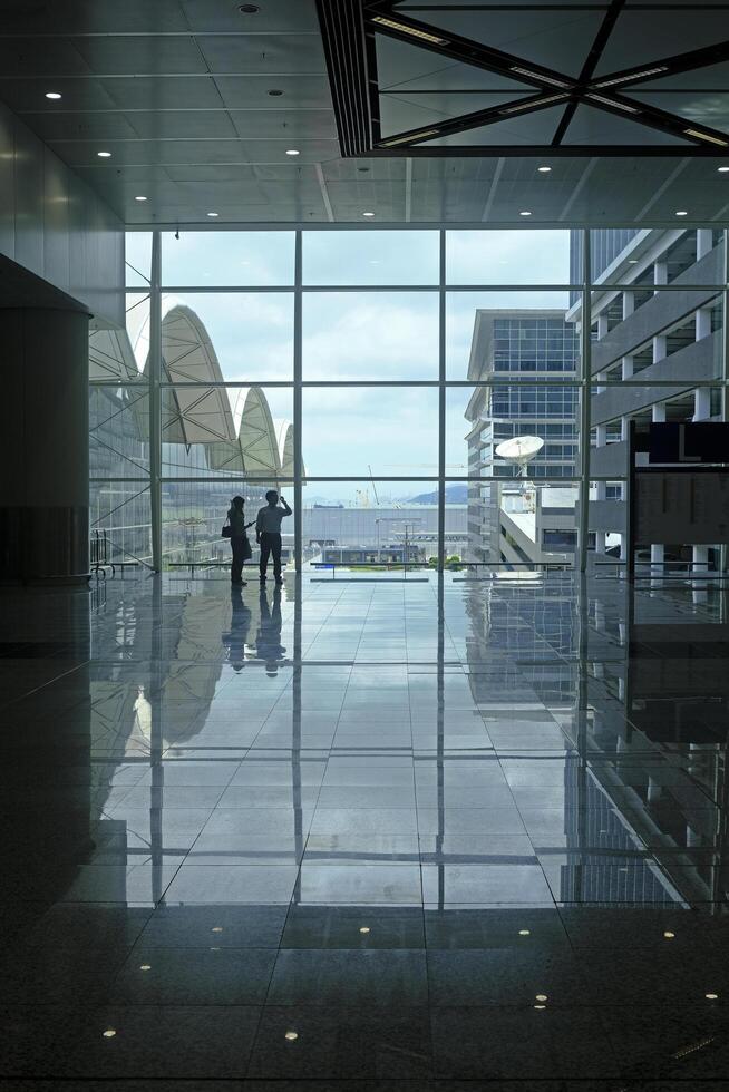 Airport terminal huge glass window with view of departure buildings and silhouette of two persons photo