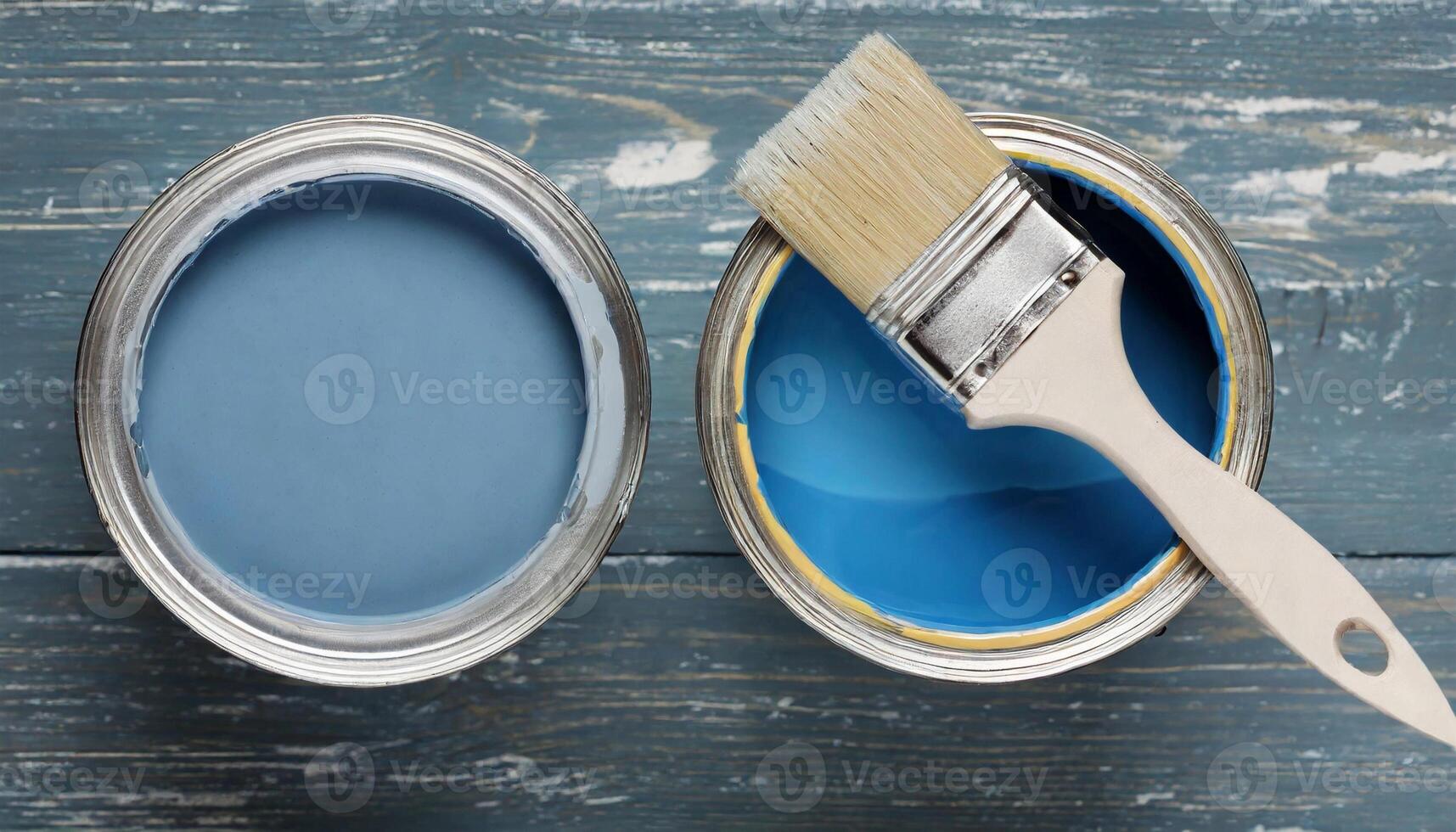 Two open cans with blue paint and construction brush on wooden background. Flat lay photo