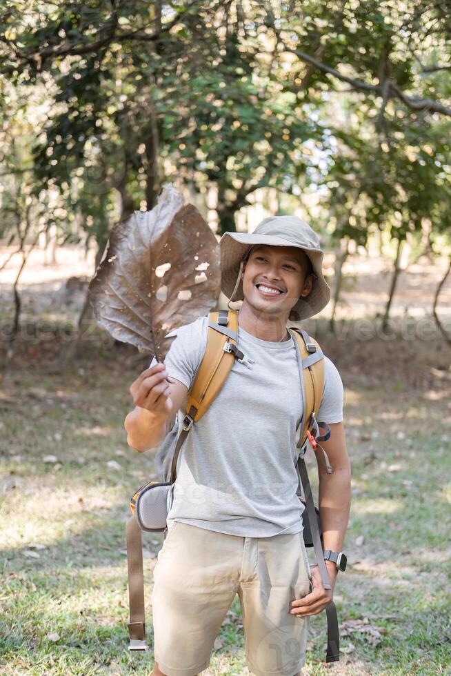 Young Man Enjoying a Hike in the Forest Holding a Large Leaf and Smiling on a Sunny Day photo