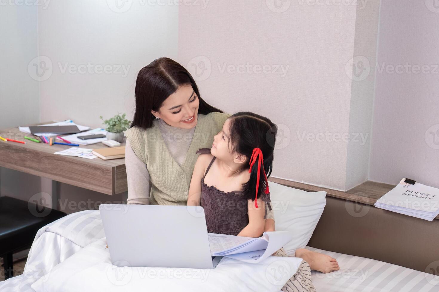 Mother and Daughter Sitting Together on Bed Working from Home with Laptop and Papers in Cozy Modern Bedroom photo