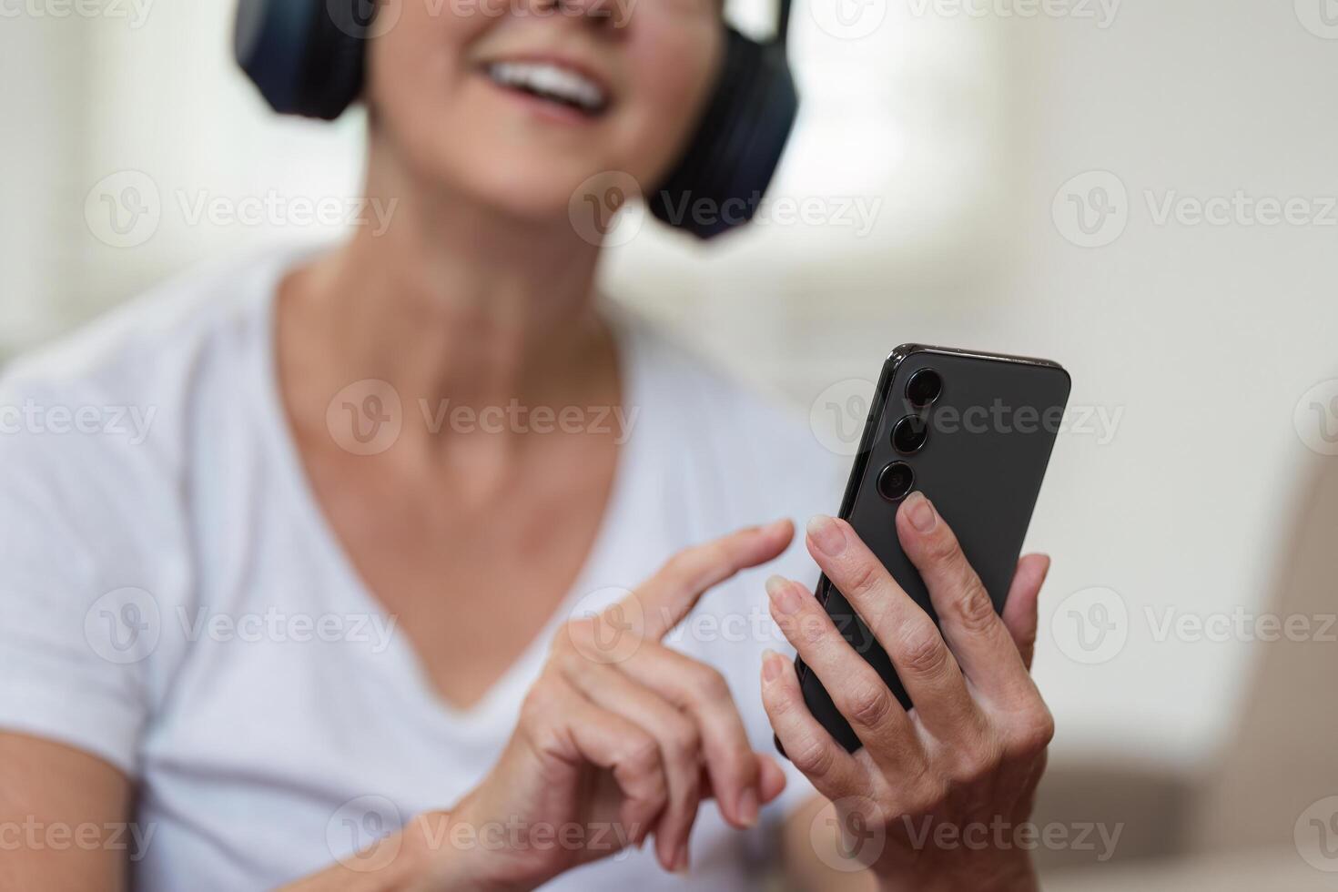 Elderly Woman Relaxing at Home and Exploring Social Media on Smartphone with Headphones photo