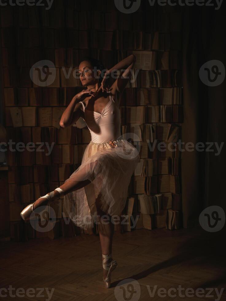 Ballerina in pointe shoes against a bookshelf. Ballet poses photo