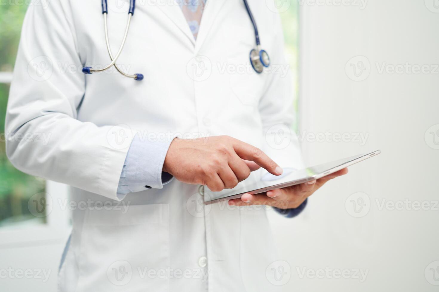 Asian man doctor using tablet computer to reading patient report, check up and search for solve treatment health medical online in hospital. photo