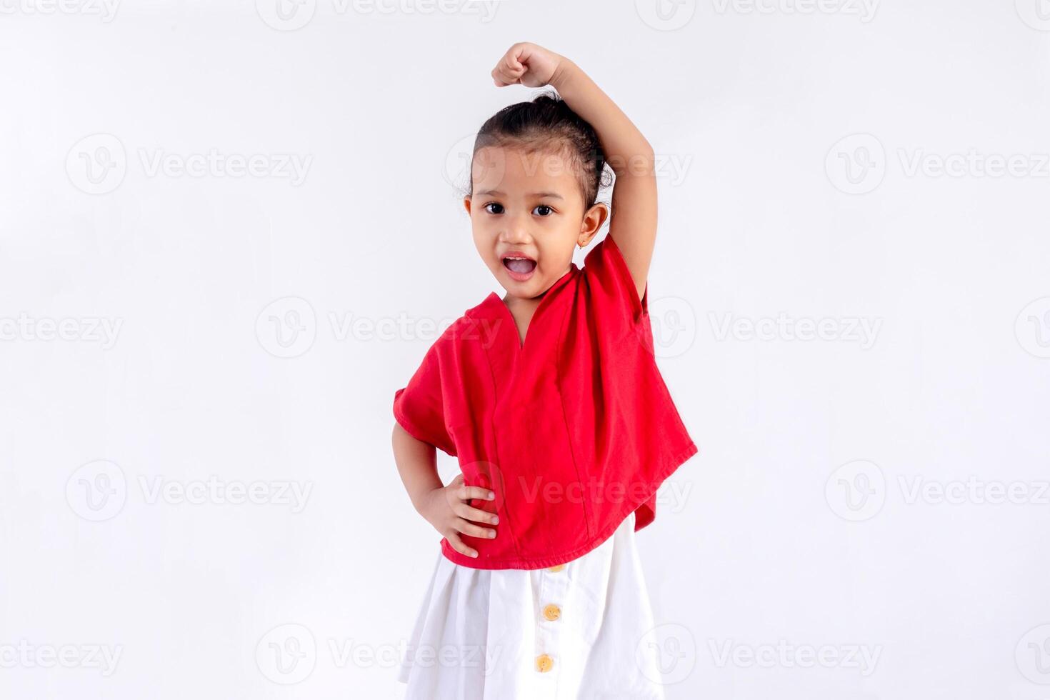 Excited little Asian girl posing with one hand on her waist and the other raised up. Indonesian Independence day concept. photo