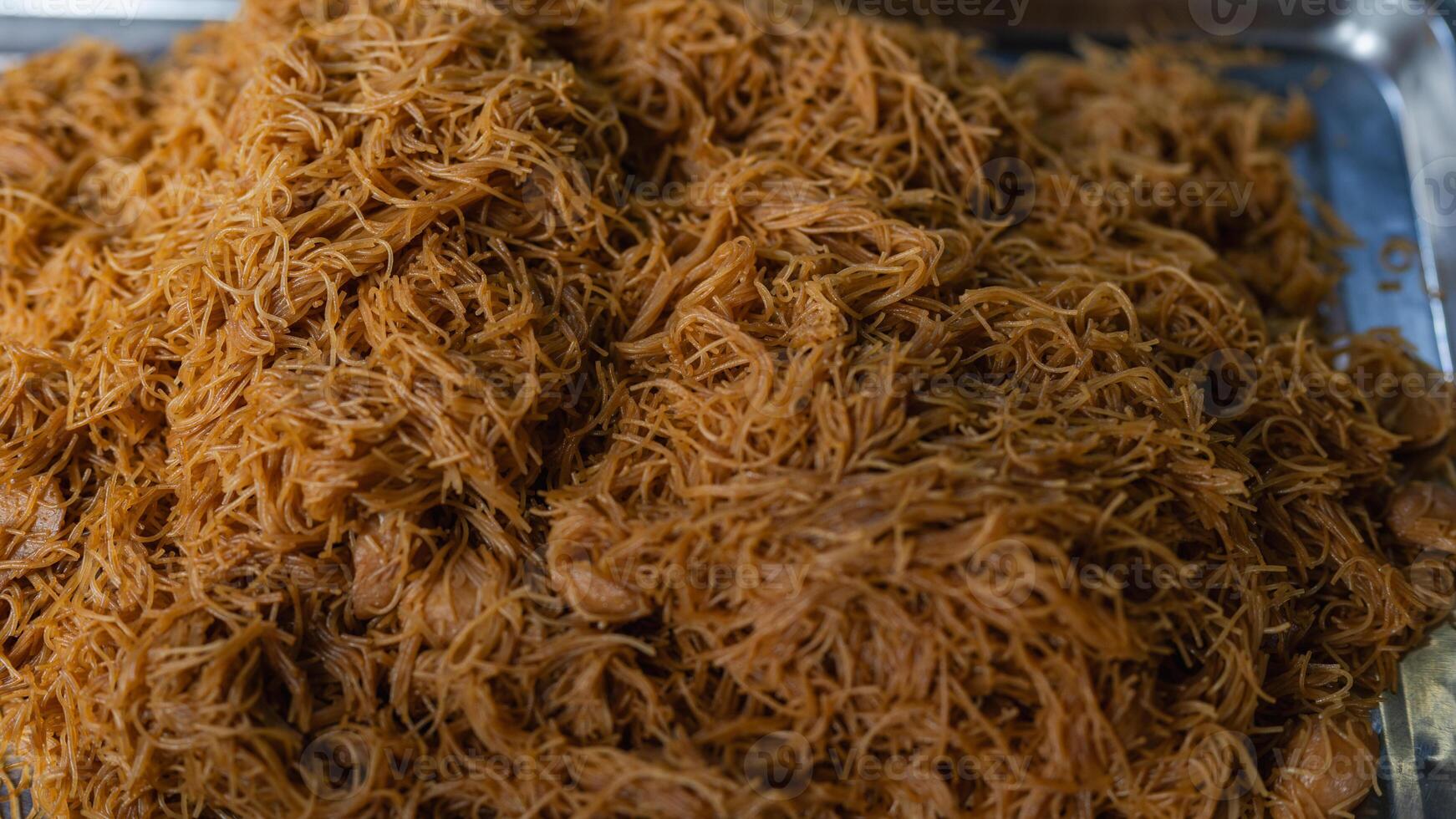 A pile of noodles is piled on top of each other. The noodles are brown and appear to be cooked photo