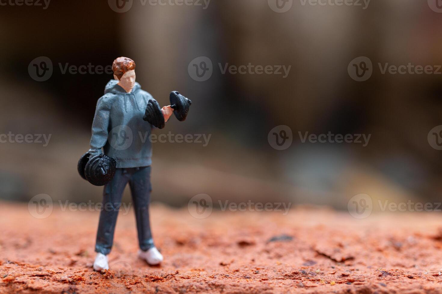 Miniature people, A man lifting dumbbells is set against a textured background photo